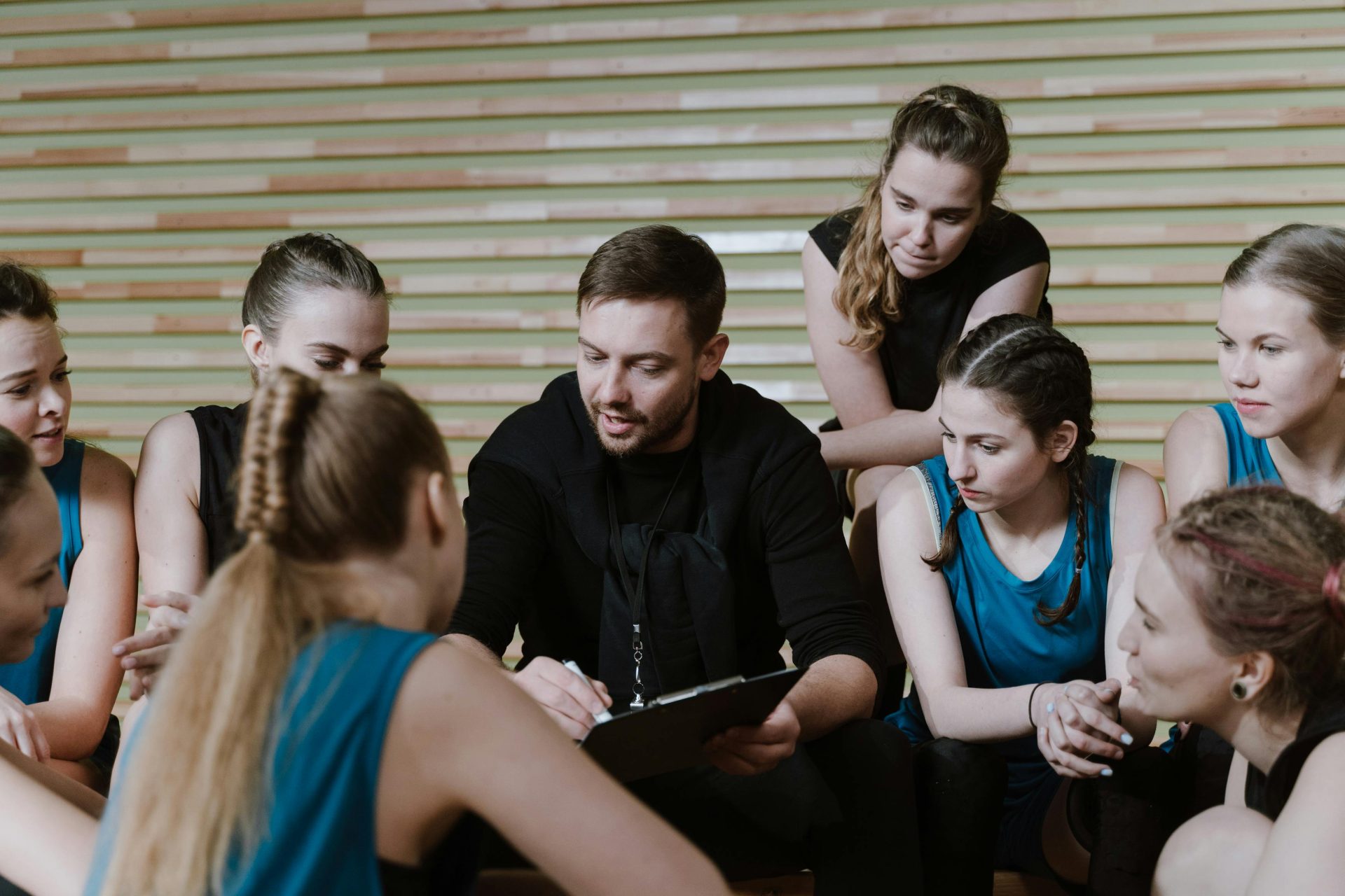 Ein Trainer bespricht die Strategie mit einer Frauenmannschaft, die in einer Turnhalle sitzt.